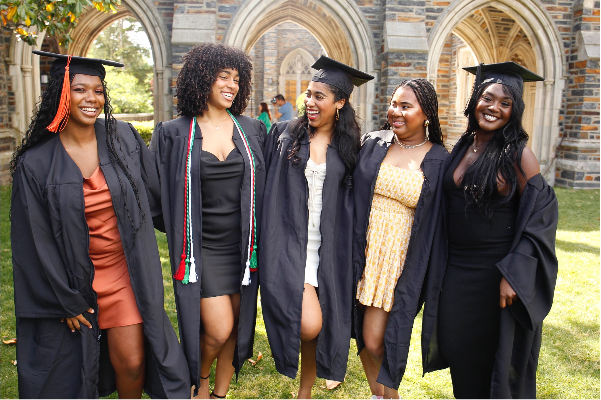 5 students in graduation garb pose for a photo outside of Page Auditorium